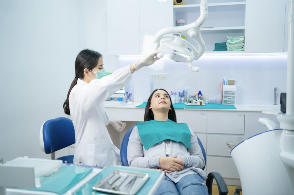 Asian female dentist adjust dental surgical light then start checking or examining tooth of patient